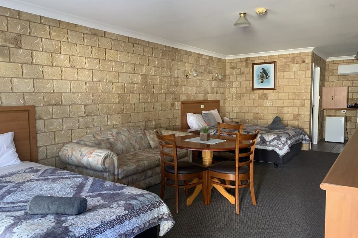 Una habitación con pared de ladrillos, una cama, un sofá, una mesa de comedor con sillas y una pequeña cocina americana.
