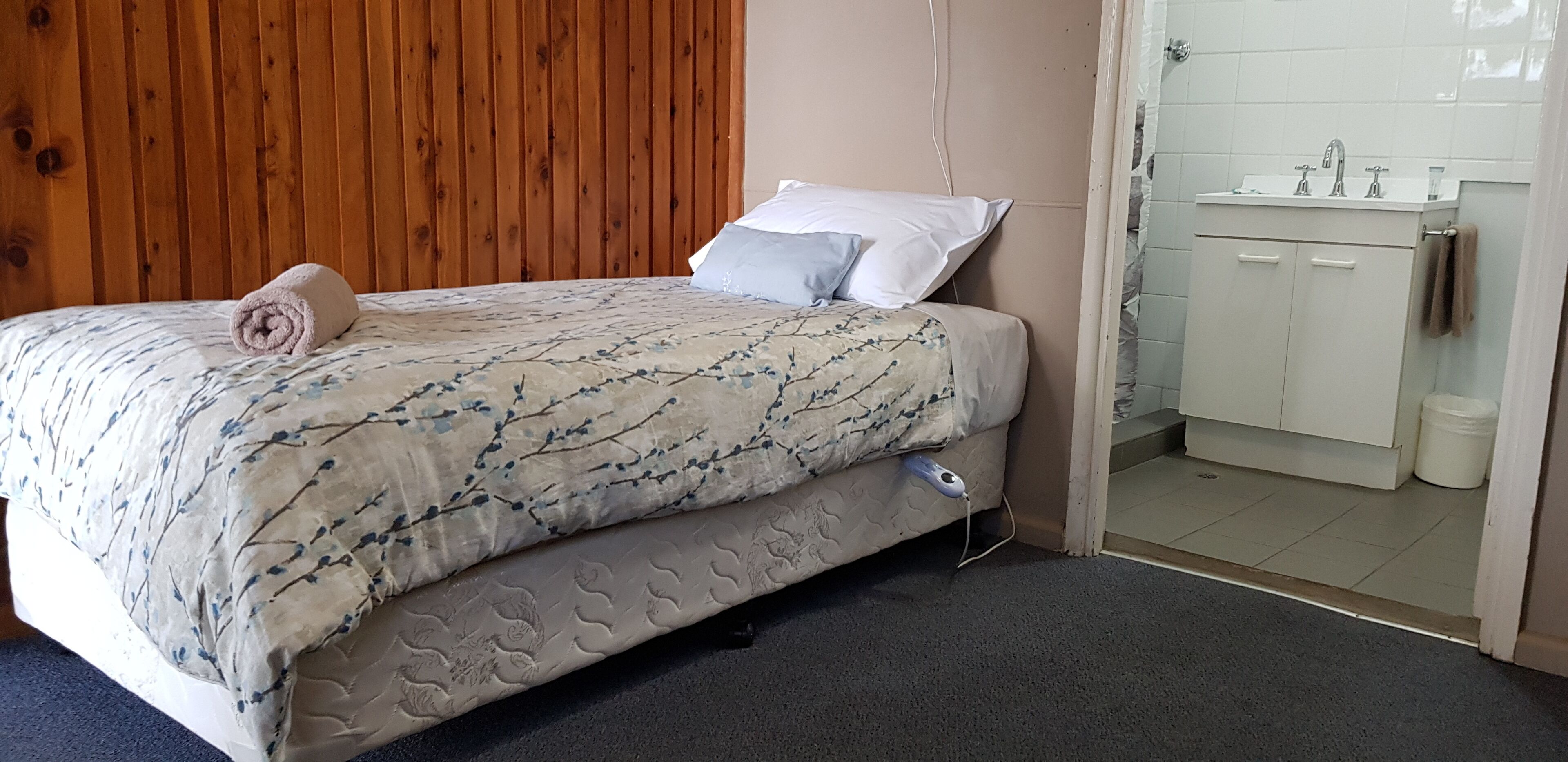 A bedroom with a bed, a wooden headboard, a bathroom with a sink and cabinets.