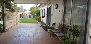 A paved pathway leading to a house with a covered porch, a fenced yard, and potted plants.