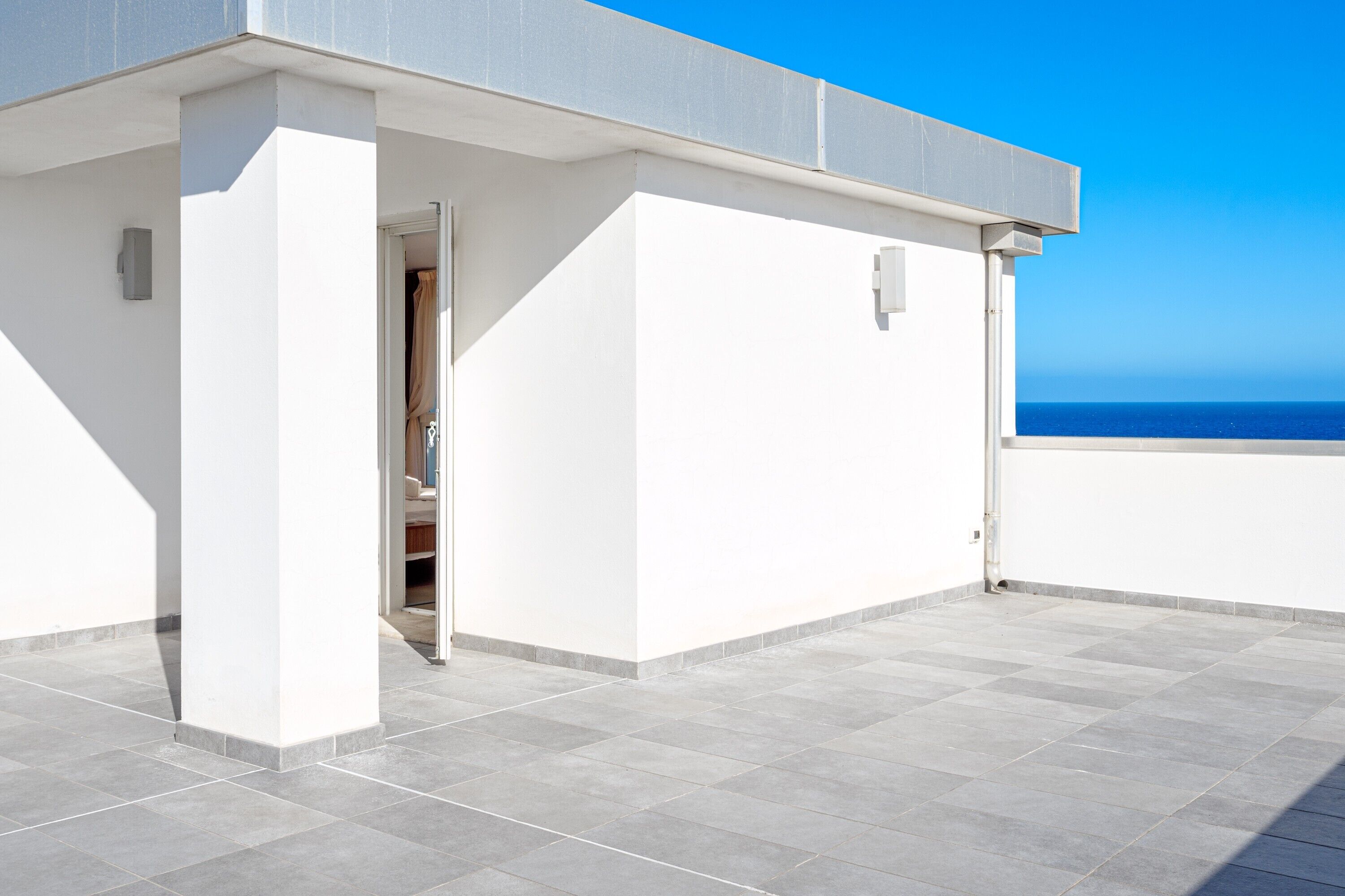 Una terraza en la azotea con vistas despejadas al mar, un edificio blanco y una puerta que da a un espacio interior.