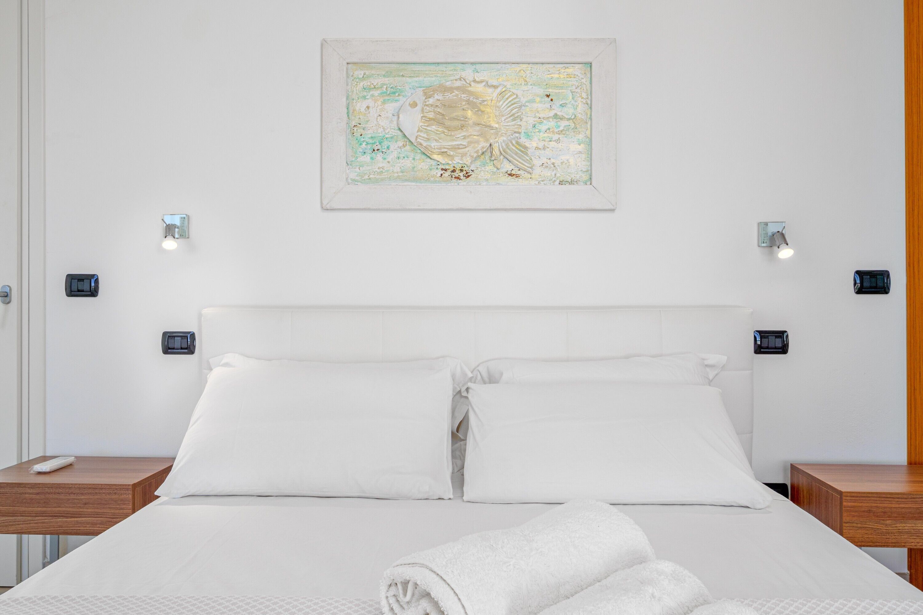 Habitación de hotel con cama, dos mesitas de noche, una obra de arte colgada en la pared y dos interruptores de luz.