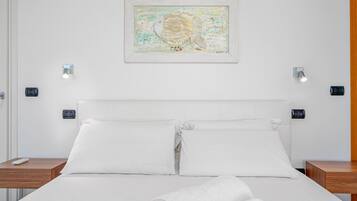 Habitación de hotel con cama, dos mesitas de noche, una obra de arte colgada en la pared y dos interruptores de luz.