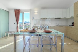 Eine moderne Küche mit einem Glastisch, transparenten Stühlen, weißen Schränken und Blick auf die Stadt.