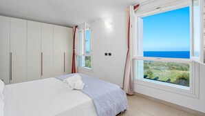 Une chambre à coucher avec un lit, une armoire, une fenêtre donnant sur la mer et un petit balcon.