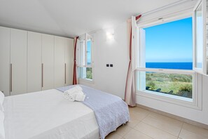 Une chambre à coucher avec un lit, une armoire, une fenêtre donnant sur la mer et un petit balcon.