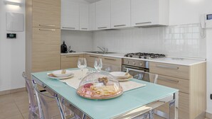 Une cuisine moderne avec des meubles blancs, une table à manger en verre et une cuisinière.