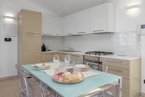 Une cuisine moderne avec des meubles blancs, une table à manger en verre et une cuisinière.