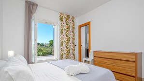 A bedroom with a bed, a wooden dresser, a desk, and a window with a view of greenery. - Unique Holiday Apartment "Villa Marconi 8" with Sea View & Spacious Sun Terrace (Golfo Aranci)