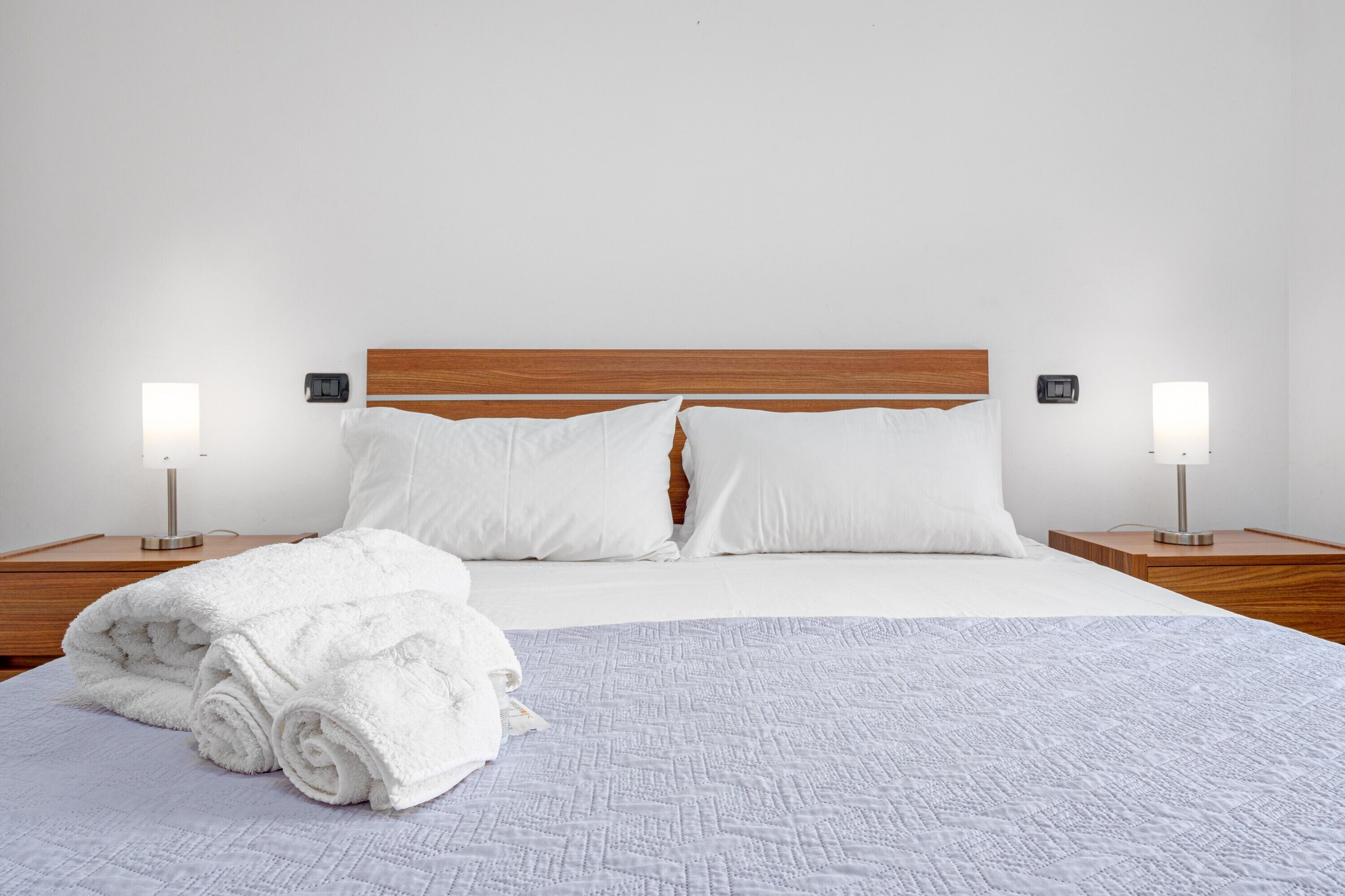 Una cama bien hecha con sábanas blancas, dos lámparas de noche y un cabecero de madera.