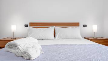 Una cama bien hecha con sábanas blancas, dos lámparas de noche y un cabecero de madera.
