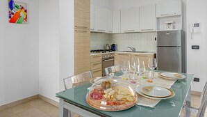 A modern kitchen with white cabinets, a stainless steel refrigerator, and a dining table set with plates, glasses, and a glass-top table. - Unique Holiday Apartment "Villa Marconi 8" with Sea View & Spacious Sun Terrace (Golfo Aranci)