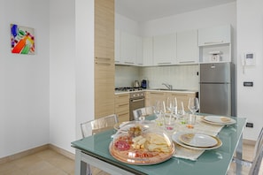 A modern kitchen with white cabinets, a stainless steel refrigerator, and a dining table set with plates, glasses, and a glass-top table.
