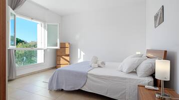 Une chambre à coucher avec un lit, une table de chevet avec une lampe, une fenêtre avec des rideaux et une vue sur la verdure à l’extérieur.