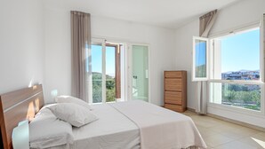 Ein Schlafzimmer mit Bett, Nachttischen, einem Schminktisch und einem großen Fenster mit Ausblick.