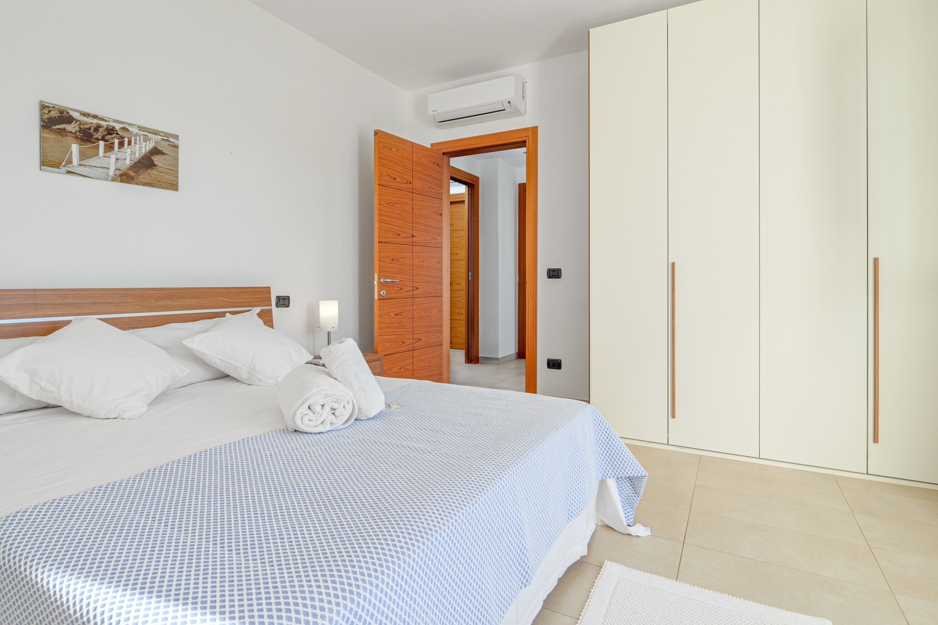 Un dormitorio con cama, un armario de madera, una pared blanca y un cuadro.