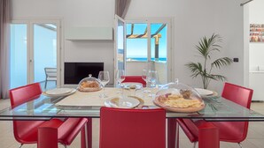 Ein Essbereich mit einem Glastisch, roten Stühlen und Blick auf das Meer durch große Fenster.
