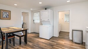 A compact kitchen with a built-in washer and dryer, a dining table with chairs, and a small trash bin.
