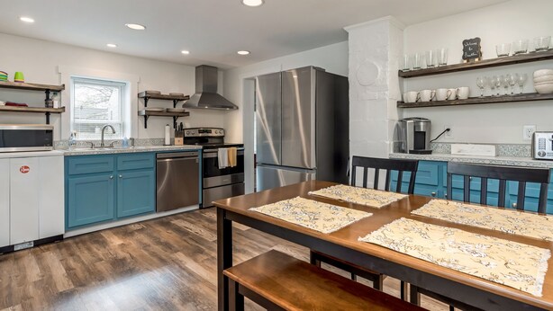 A modern kitchen with teal cabinets, stainless steel appliances, and a wooden dining table with placemats.