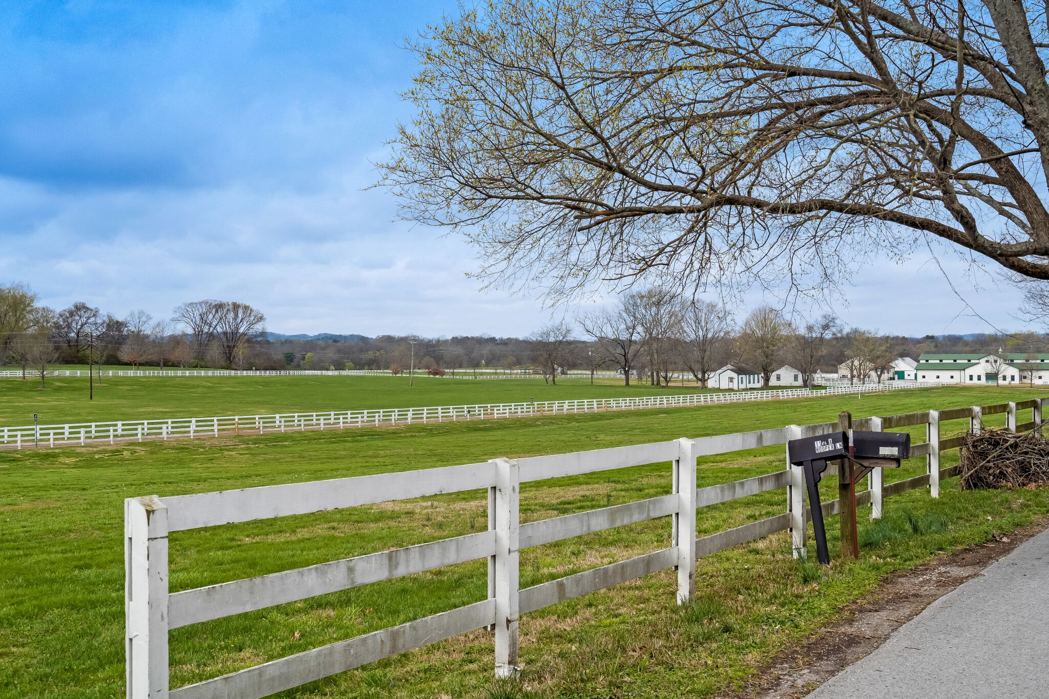 A rural landscape with a white fence, a mailbox, and a green field.
