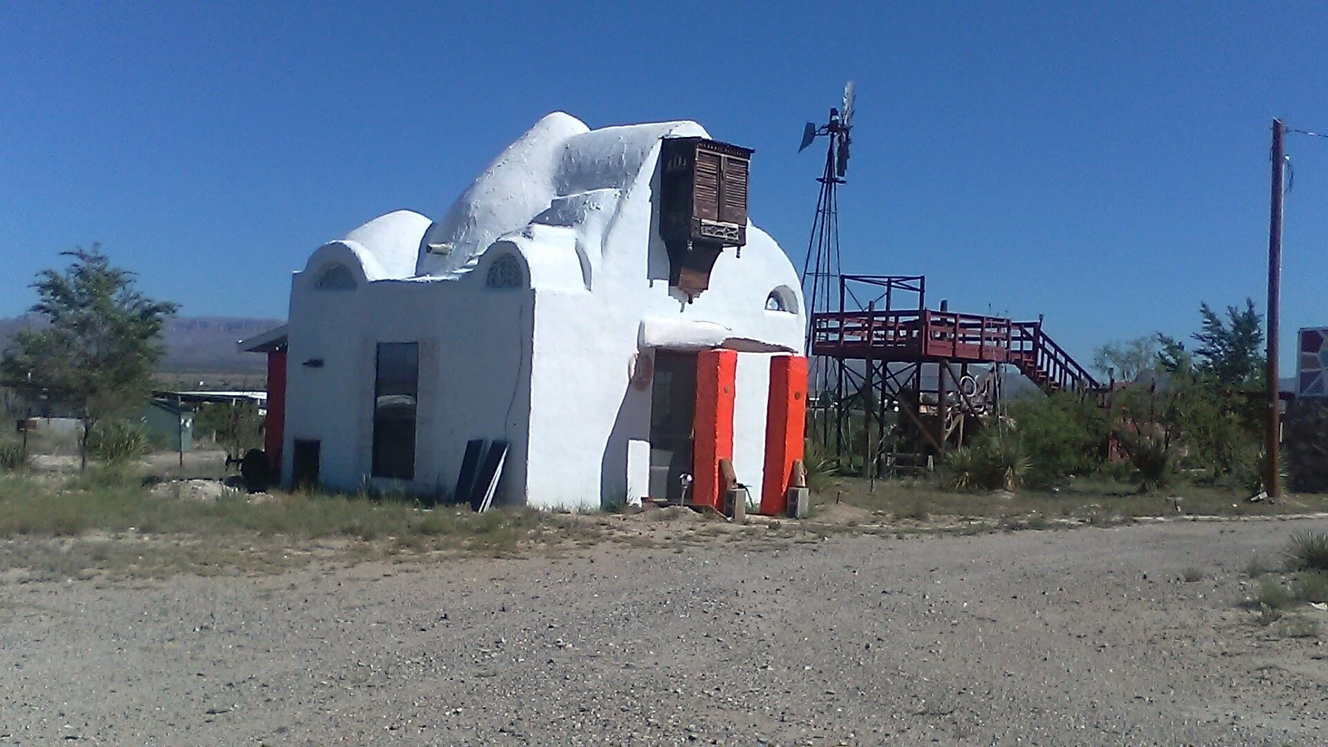 Un petit bâtiment blanc orné de rayures rouges et blanches, un moulin à vent et, au fond, une structure métallique rouge.