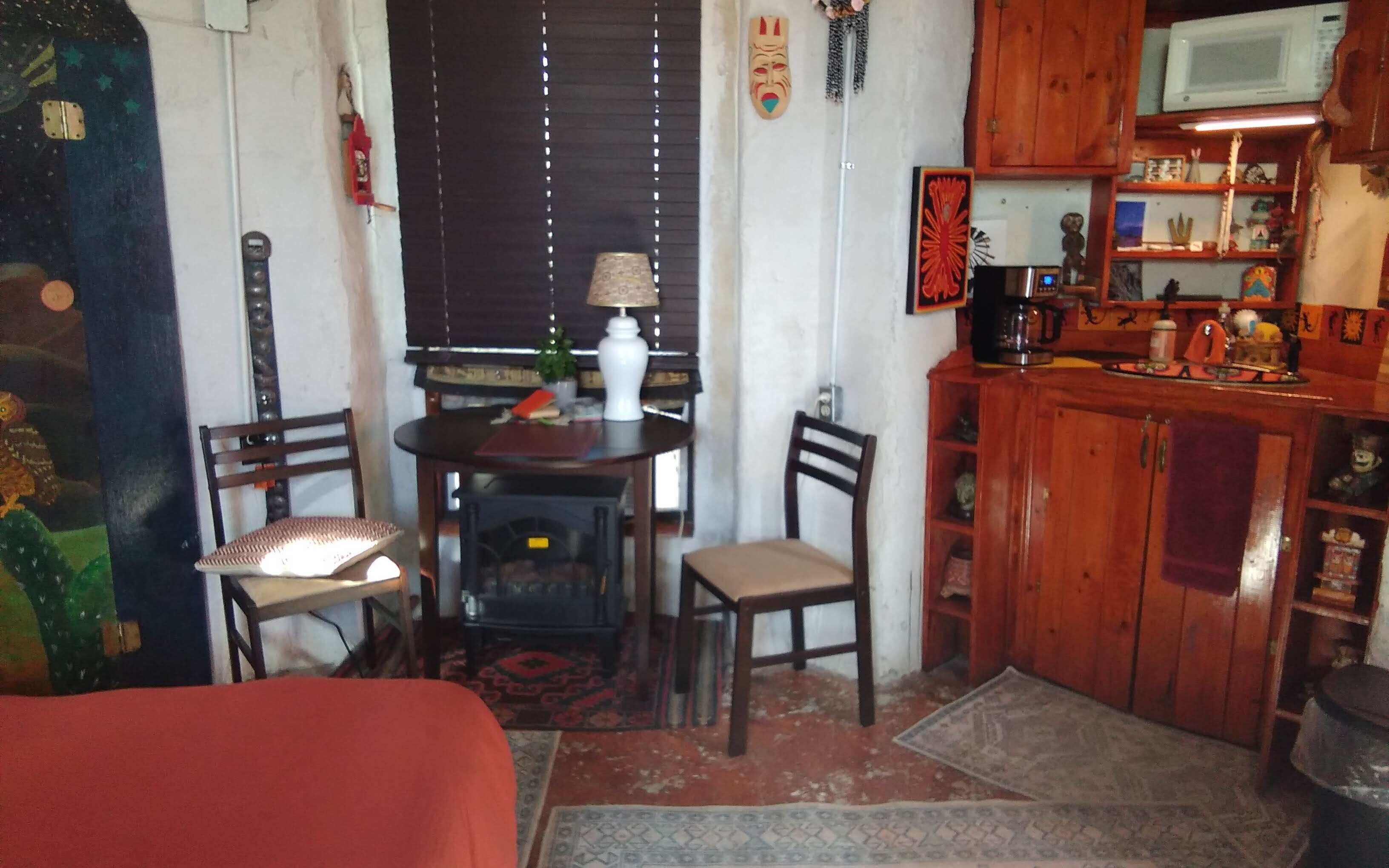 Quarto pequeno e aconchegante com uma cama, uma mesa com cadeiras, um micro-ondas e um armário com diversos objetos.