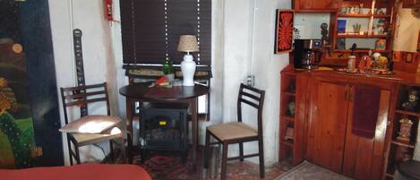 Quarto pequeno e aconchegante com uma cama, uma mesa com cadeiras, um micro-ondas e um armário com diversos objetos.