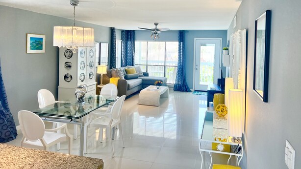 A modern living room with a glass dining table, a sofa, and a ceiling fan. - Lux Long Term Condominium (South Padre Island)
