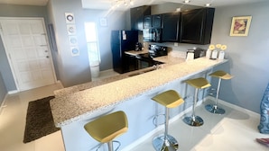 A modern kitchen with a bar area, stainless steel appliances, and a white countertop. - Lux Long Term Condominium (South Padre Island)