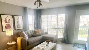 A modern living room with a grey sofa, a white coffee table, and a floor lamp. - Lux Long Term Condominium (South Padre Island)