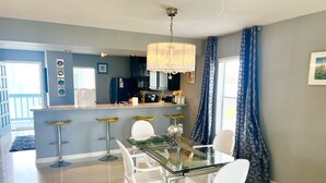 A modern kitchen with a glass dining table, white chairs, and a bar area with stools. - Lux Long Term Condominium (South Padre Island)