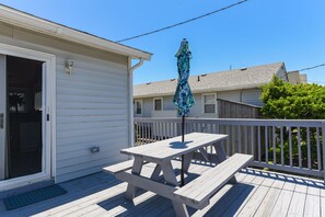 A wooden deck with a picnic table and umbrella, a sliding door, and a white railing. - Blackbird Inn: Oceanside, Pet-friendly, Close to Beach, Short Stays Anytime! (Kill Devil Hills)