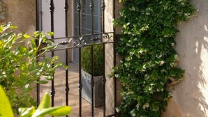 A wrought iron gate with a climbing vine and white flowers, leading to a building with a stone facade and a window.