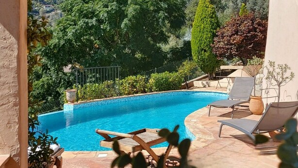 A pool with lounge chairs and a view of a hillside with houses.