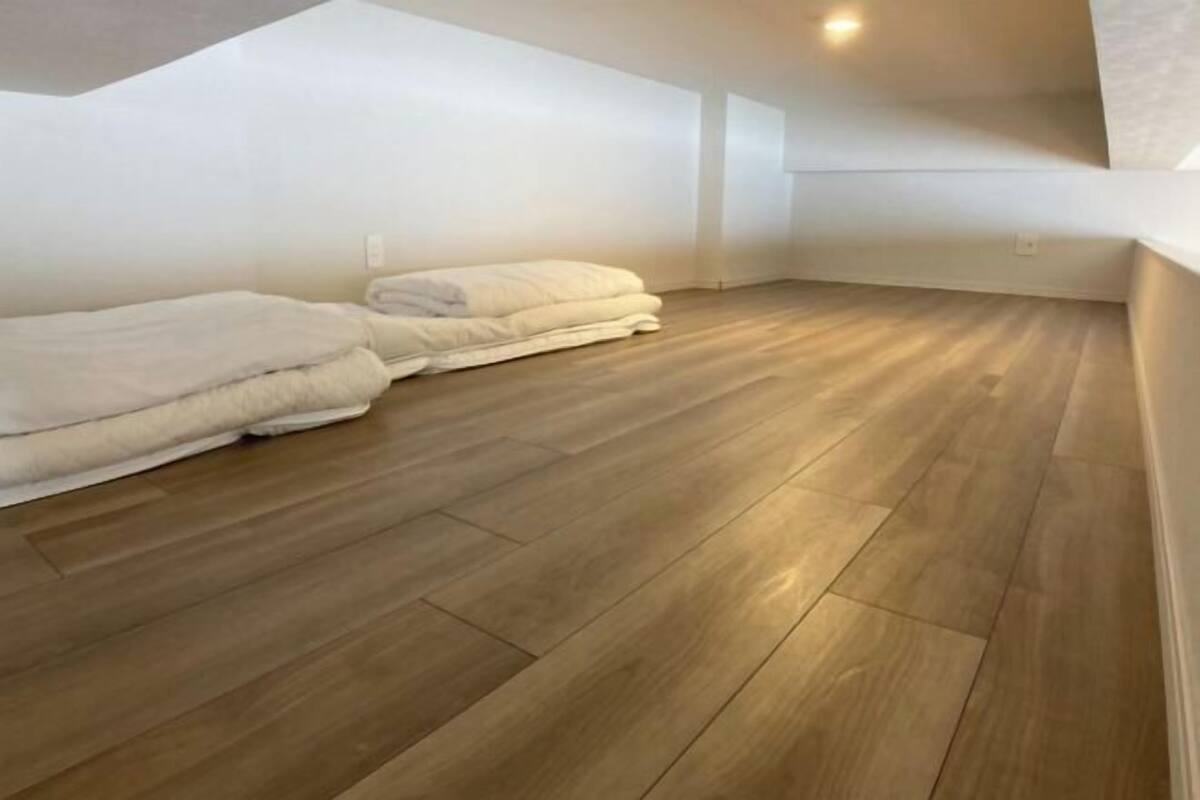 Een kamer met een schuine kap, houten vloer en twee keurig opgevouwen witte dekens.