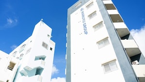 Een modern gebouw met een witte gevel en blauwe accenten, met meerdere balkons en een heldere lucht op de achtergrond.