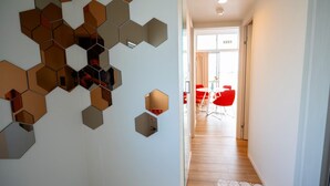 Een gang met hexagonale spiegels aan de muur, die leidt naar een eetgedeelte met rode stoelen en een tafel.