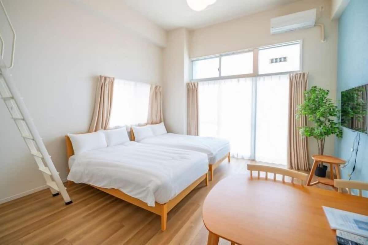 Een slaapkamer met twee bedden, een houten vloer, een kleintje tafeltje en een raam met gordijnen.