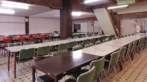 A conference room with long tables and green chairs, wooden beams on the ceiling, and a clock on the wall. - Shintaku Sanso (Minamimaki)
