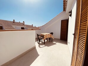 A small outdoor balcony with a table and chairs, a tiled floor, and a view of neighboring buildings.