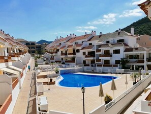 A resort with a central swimming pool, white buildings with red-tiled roofs, and a clear sky.