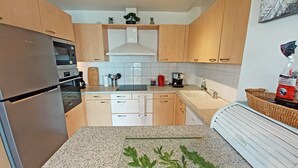 A modern kitchen with wooden cabinets, a stainless steel refrigerator, a built-in oven, a sink, and a countertop with a cutting board and utensils. - T3 of 68 m2 in Porticcio. Covered terrace 20 m2, small garden 50 m2. Walking distance to the beach. (Grosseto-Prugna)