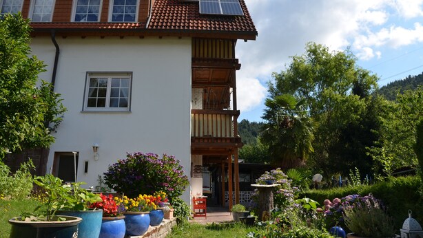 A two-story house with a balcony, solar panels on the roof, and a garden with various potted plants and flowers. - Family-friendly, Black Forest Nature Park Murg Valley Baden Baden Hiking vacation  (Weisenbach)