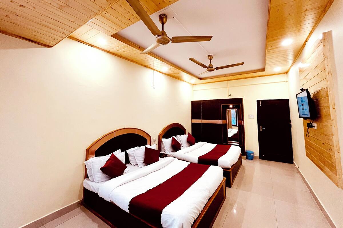 A hotel room with two beds, wooden ceiling, ceiling fans, a TV mounted on the wall, and a door leading to another room.