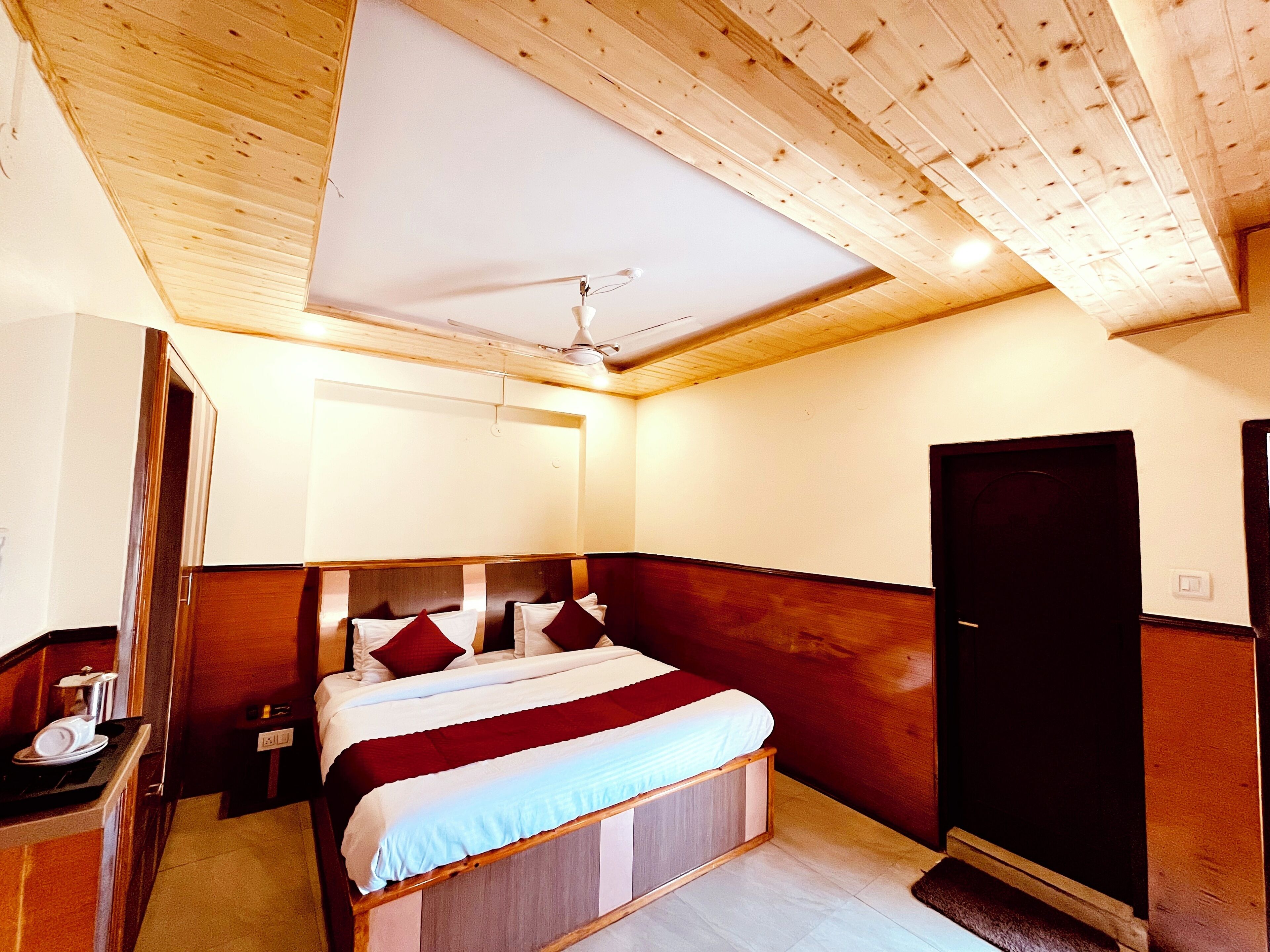 A bedroom with a wooden ceiling, a bed with red and white bedding, a nightstand, and a wardrobe.