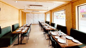 Une longue salle à manger aux murs et au plafond en bois, avec des banquettes recouvertes d’un tissu vert et des tables dressées avec des assiettes et des couverts.
