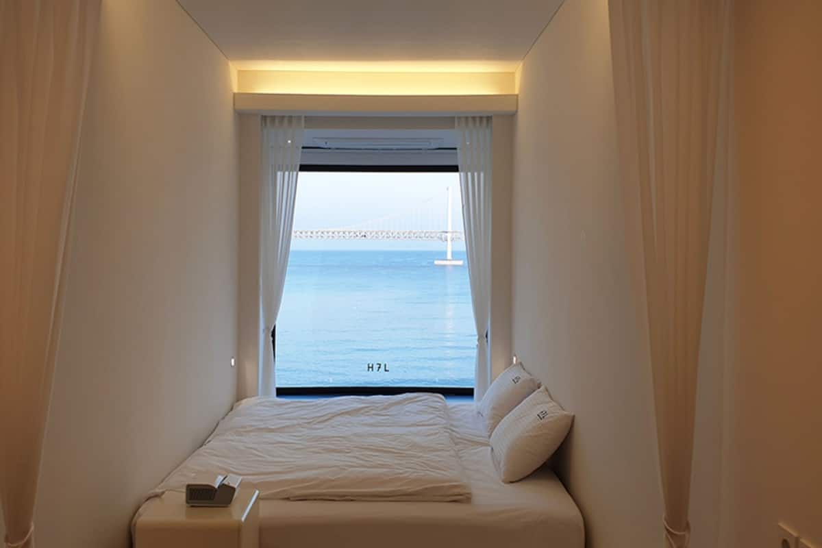 A hotel room with a bed, a laptop, and a view of the sea and a bridge.
