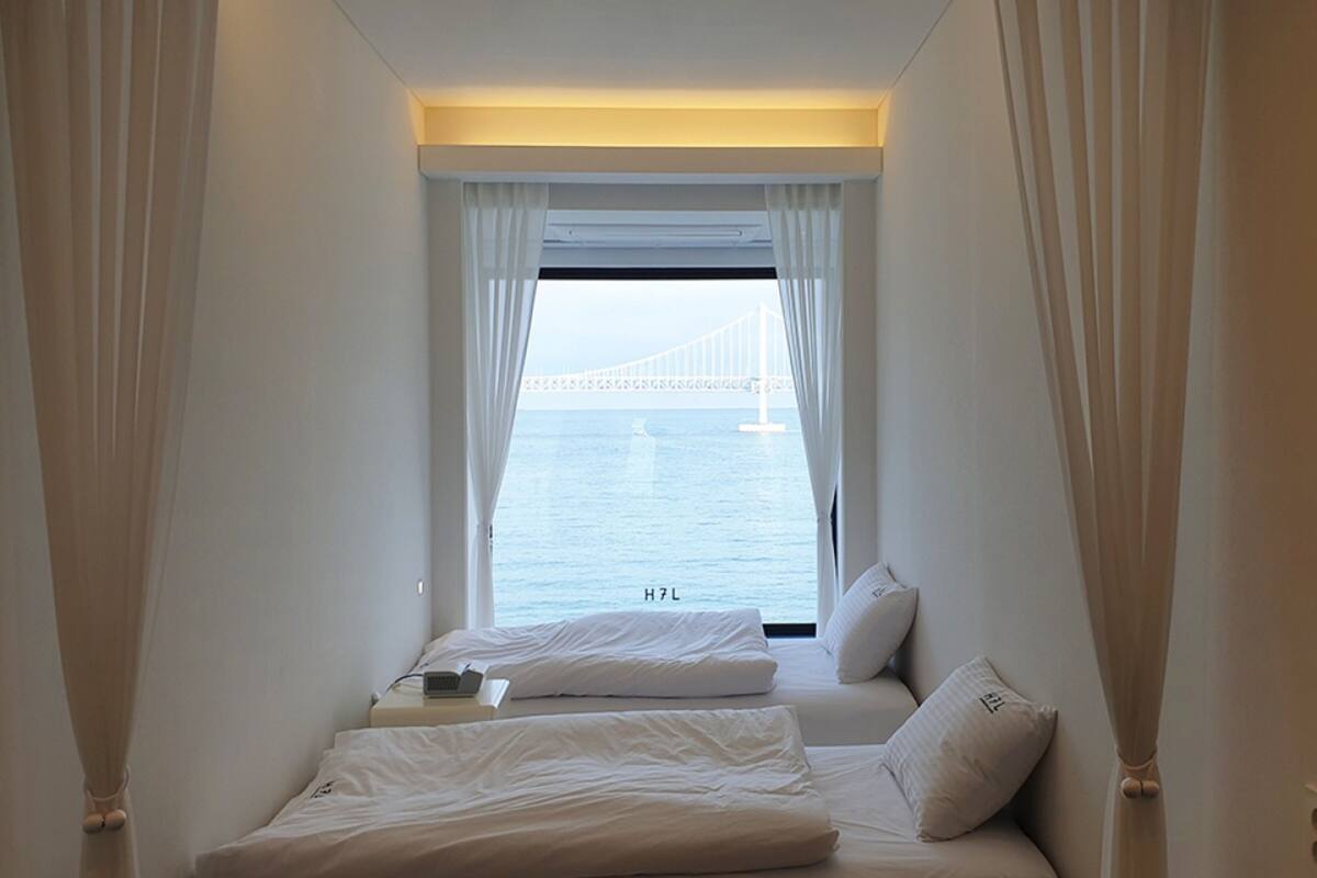 A room with two beds, a laptop on one bed, and a view of a bridge over water.