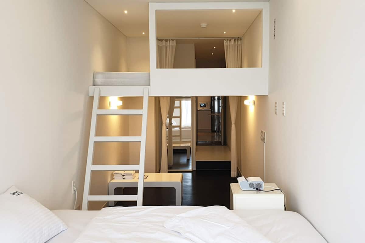 A bunk bed room with a desk and a phone on a bedside table.