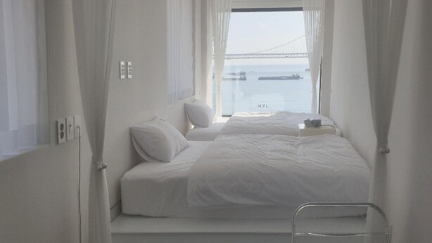 A hotel room with two beds, a view of a bridge, and a window with curtains.