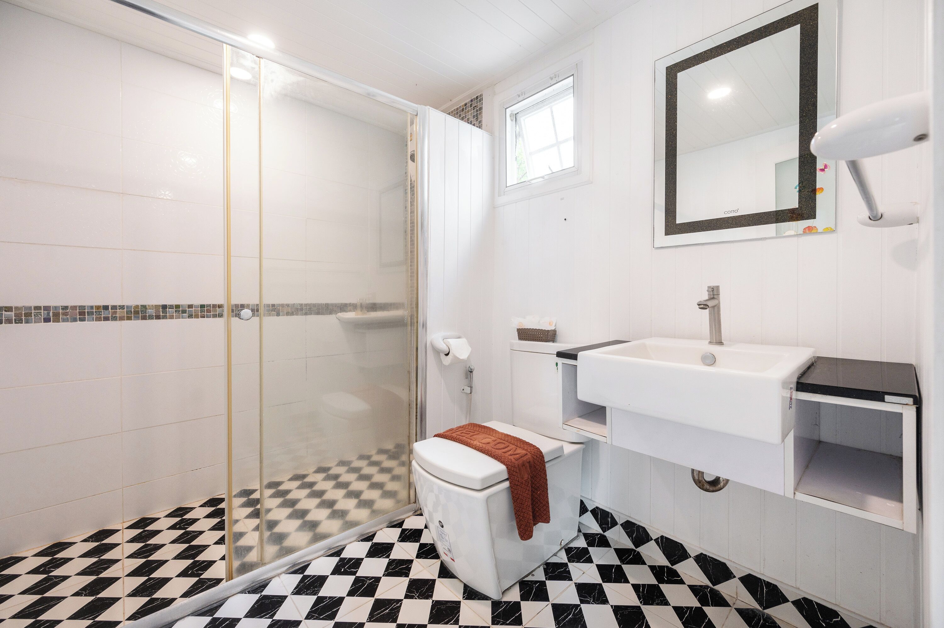 A bathroom with a glass-enclosed shower, a toilet with a towel, a sink, and a mirror.